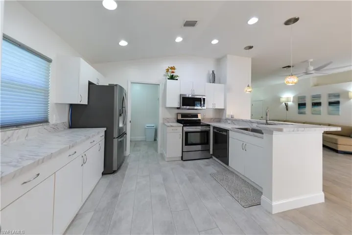 Kitchen with stainless steel appliances, kitchen peninsula, light hardwood / wood-style flooring, lofted ceiling, and pendant lighting