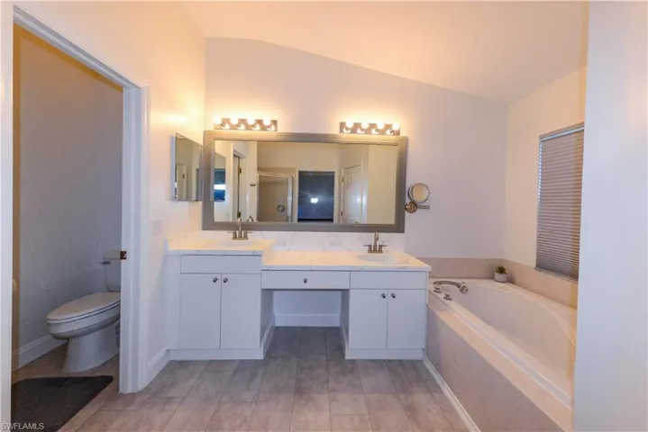 Bathroom with wood-type flooring, tiled tub, vanity, toilet, and lofted ceiling