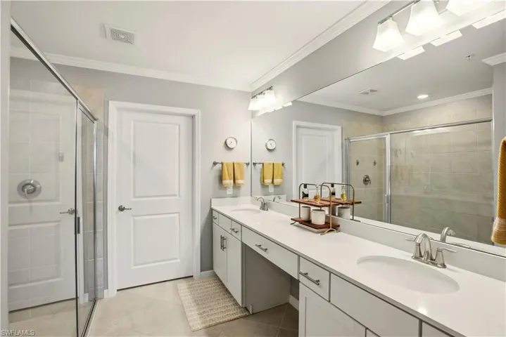 Bathroom featuring double vanity, ornamental molding, a stall shower, and light tile patterned floors