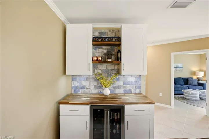 Indoor dry bar with butcher block countertops, crown molding, wine cooler, white cabinetry, and tasteful backsplash