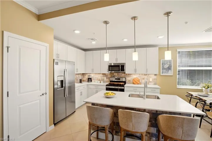 Kitchen with stainless steel appliances, white cabinets, a center island with sink, pendant lighting, and a breakfast bar