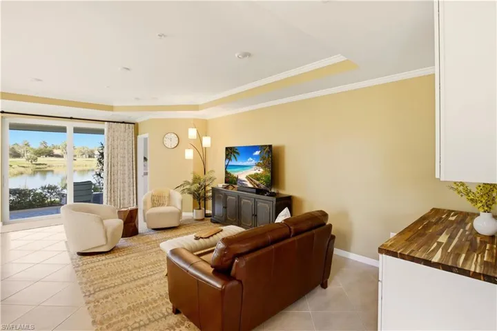 Living area with light tile patterned floors, a water view, crown molding, and a tray ceiling