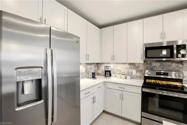 Kitchen featuring stainless steel appliances, white cabinets, light tile patterned floors, and backsplash
