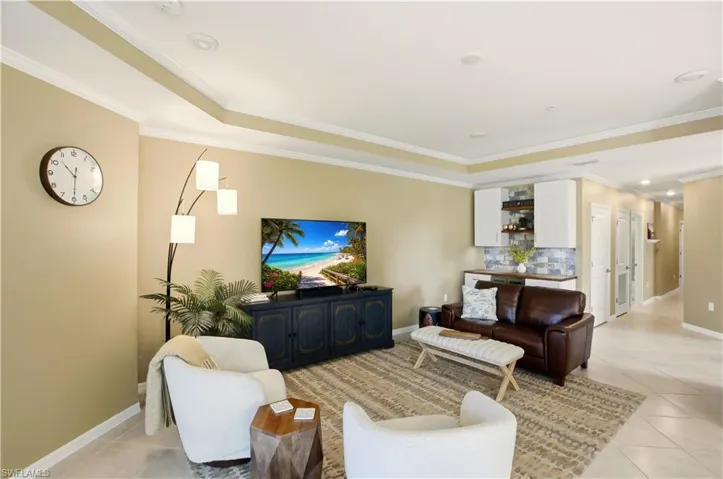 Living room with light tile patterned floors, ornamental molding, and a raised ceiling