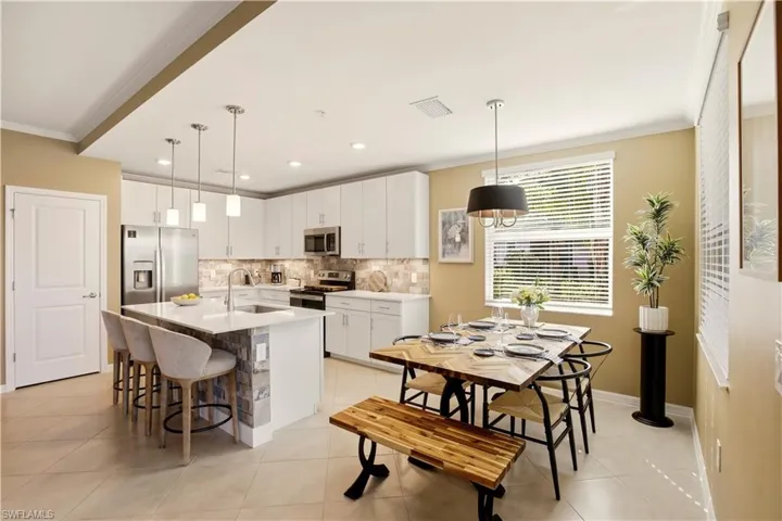 Kitchen with crown molding, white cabinetry, stainless steel appliances, a kitchen breakfast bar, and a kitchen island with sink