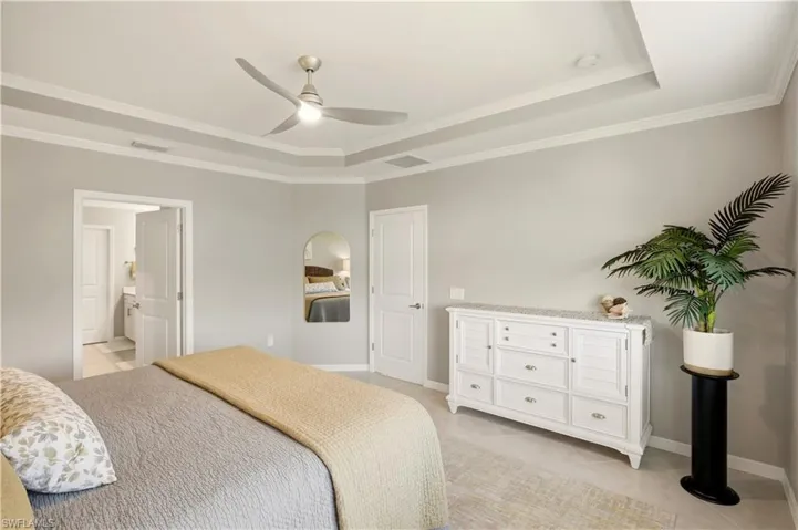 Bedroom with a ceiling fan, a raised ceiling, ornamental molding, and ensuite bathroom