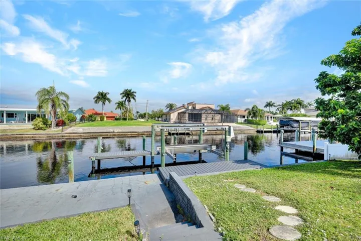 Dock with a water view, boat lift, a lawn, and a residential view