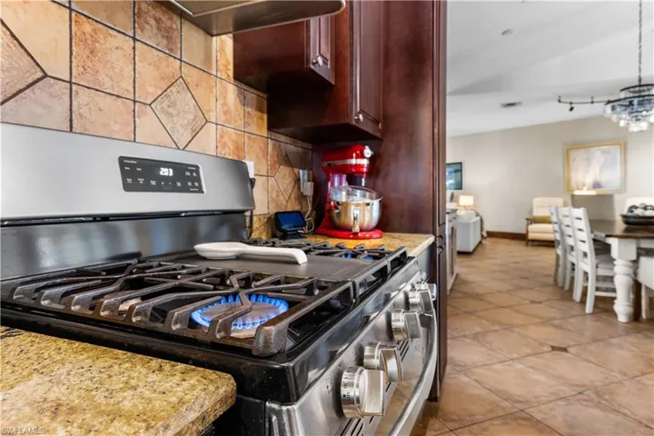 Kitchen with stainless steel range with gas stovetop, backsplash, exhaust hood, light stone countertops, and suspended lighting