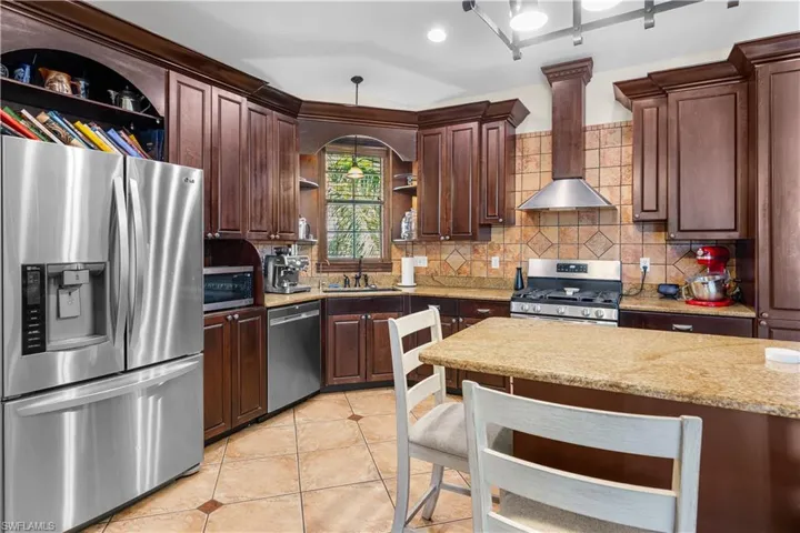 Kitchen with open shelves, stainless steel appliances, dark wood finish cabinets, pendant lighting, and a kitchen bar