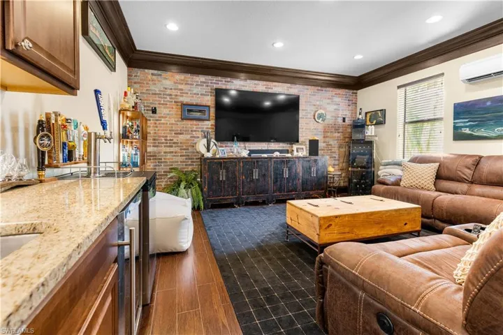 Family room with brick wall, bar with sink, wine cooler, crown molding, and an accent wall