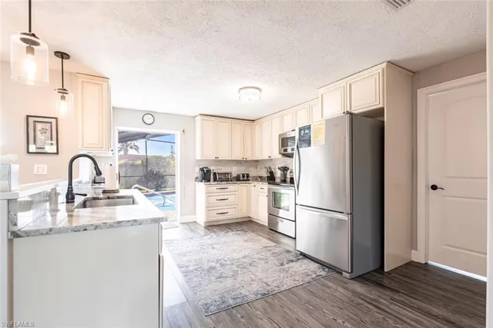 Kitchen with stainless steel appliances, cream cabinets, light stone counters, light wood finished floors, and hanging light fixtures