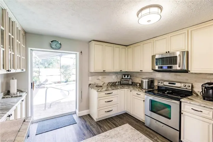 Kitchen featuring stainless steel appliances, light stone counters, a textured ceiling, dark wood-style floors, and cream cabinetry