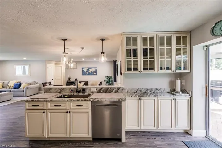 Kitchen with open floor plan, dishwasher, pendant lighting, a peninsula, and light stone counters