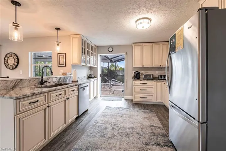 Kitchen with cream cabinetry, stainless steel appliances, decorative light fixtures, light stone counters, and glass insert cabinets