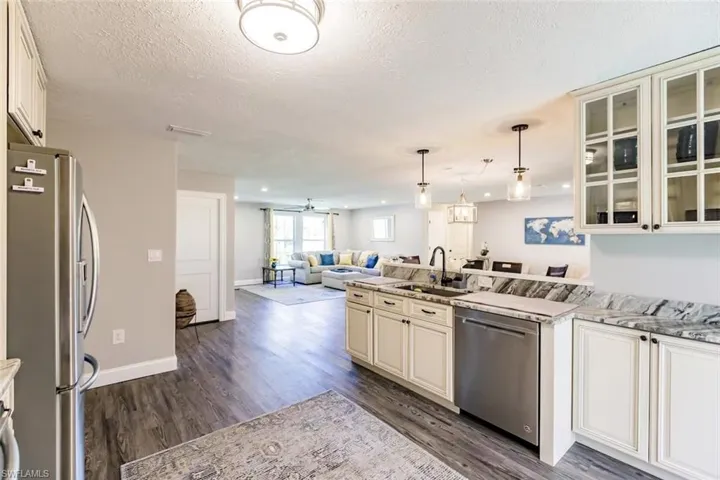 Kitchen featuring stainless steel appliances, pendant lighting, dark wood-style floors, light stone countertops, and open floor plan