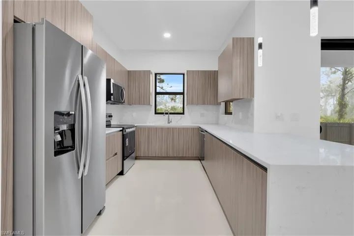 Kitchen featuring appliances with stainless steel finishes, tasteful backsplash, light stone counters, modern cabinets, and a peninsula
