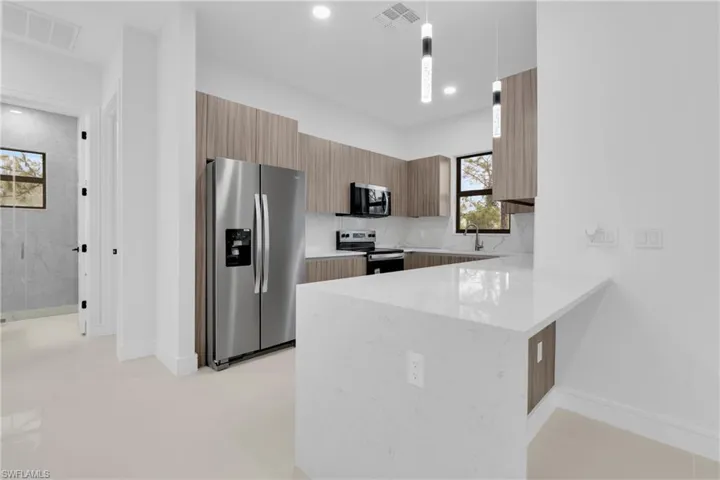 Kitchen with hanging light fixtures, stainless steel appliances, light stone countertops, modern cabinets, and a peninsula