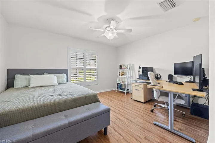 Wood-finish flooring, white walls, white ceiling fan, and window with white louvered shutters