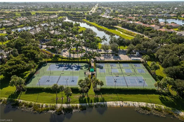 Four tennis courts with blue playing surfaces and green surrounds, bordered by lush green landscaping and mature palm trees