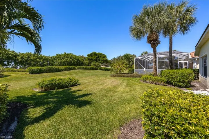 Expansive green lawn with mature palm trees and lush landscaping, featuring a screened enclosure