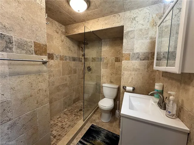 Bathroom with toilet, vanity, and tiled shower