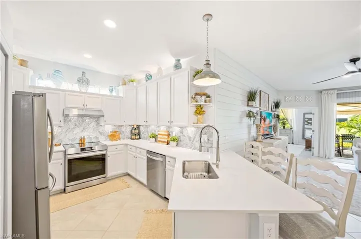 Kitchen featuring appliances with stainless steel finishes, a peninsula, under cabinet range hood, decorative backsplash, and light countertops