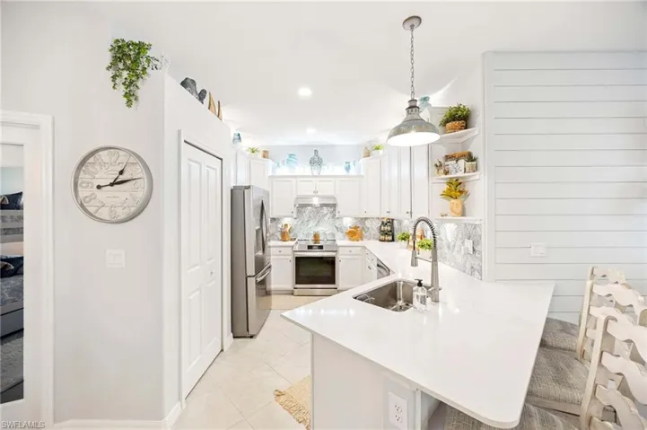 Kitchen featuring appliances with stainless steel finishes, a peninsula, under cabinet range hood, open shelves, and decorative backsplash