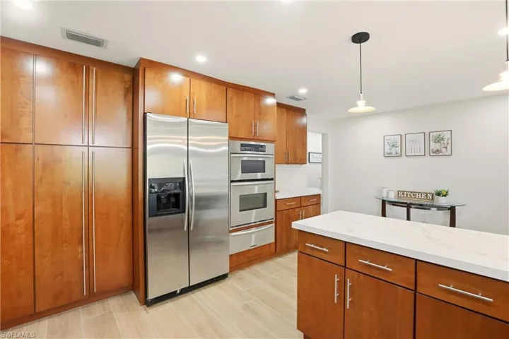Kitchen featuring brown cabinetry, appliances with stainless steel finishes, decorative light fixtures, light stone counters, and a warming drawer