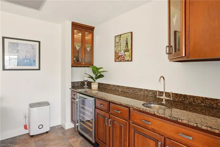Bar area with glass insert cabinets, dark stone counters, beverage cooler, and brown cabinets