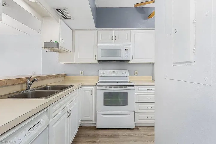 Kitchen featuring sink, light hardwood / wood-style flooring, white appliances, and white cabinetry