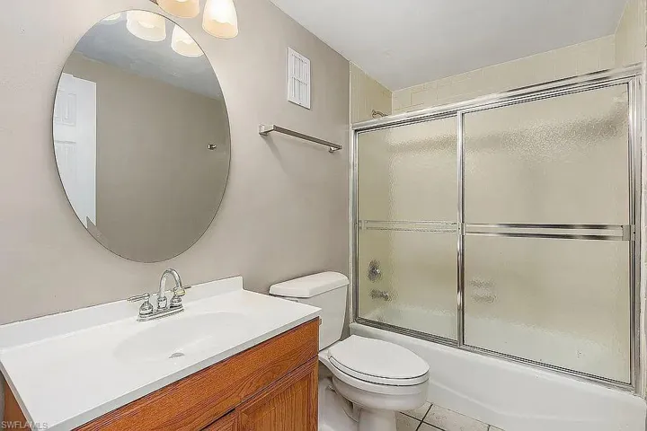Full bathroom with tile flooring, vanity, toilet, and bath / shower combo with glass door