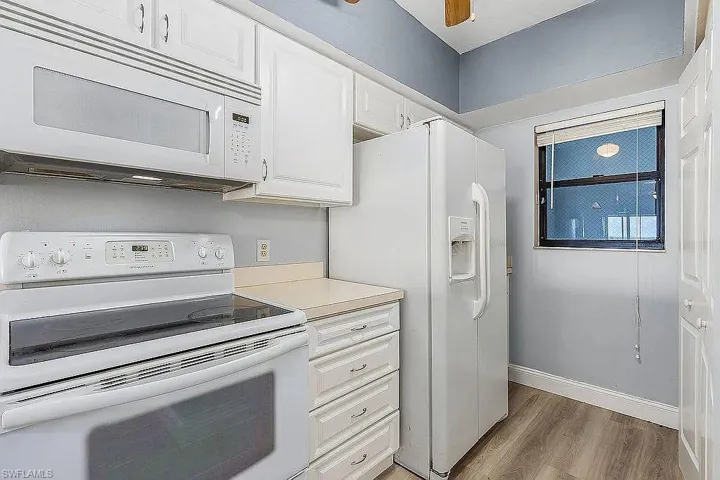 Kitchen featuring dark hardwood / wood-style flooring, white cabinets, and white appliances