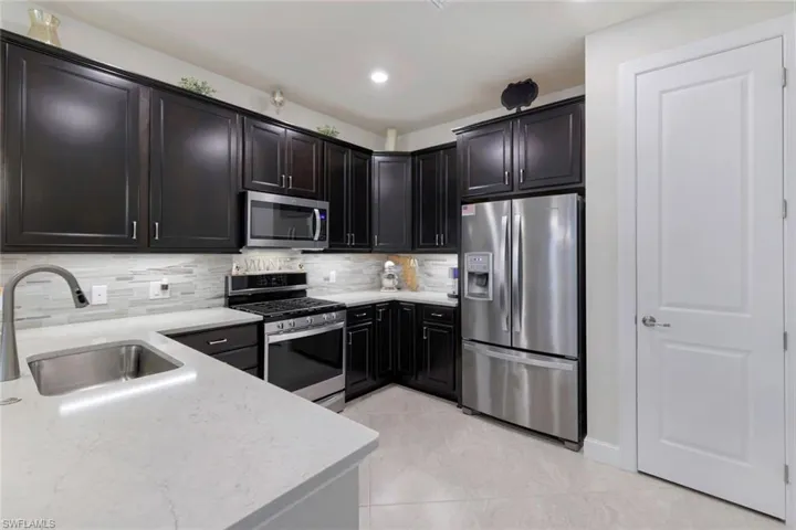 Kitchen featuring stainless steel appliances, light stone counters, decorative backsplash, sink, and light tile patterned flooring