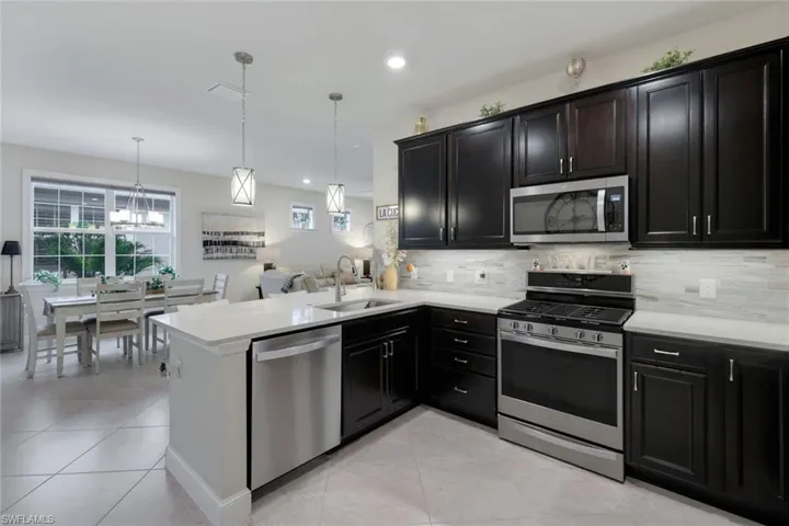 Kitchen featuring stainless steel appliances, sink, kitchen peninsula, backsplash, and hanging light fixtures