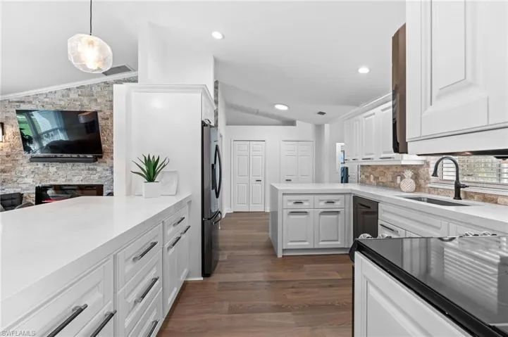 Kitchen with vaulted ceiling, a peninsula, white cabinets, dark wood-style flooring, and pendant lighting