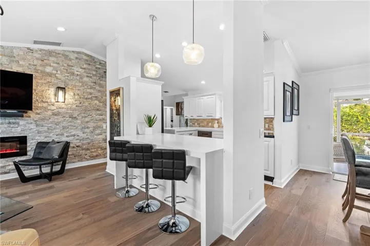Kitchen with lofted ceiling, crown molding, dark wood-style flooring, hanging light fixtures, and white cabinets