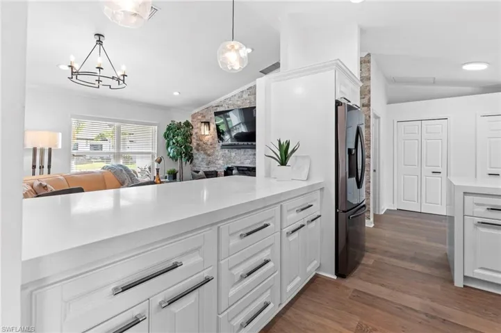 Kitchen with white cabinets, lofted ceiling, hanging light fixtures, dark wood-style flooring, and light stone countertops