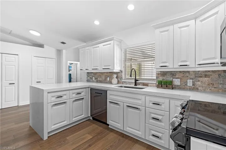 Kitchen featuring range with electric stovetop, a peninsula, light stone counters, dark wood-type flooring, and white cabinets