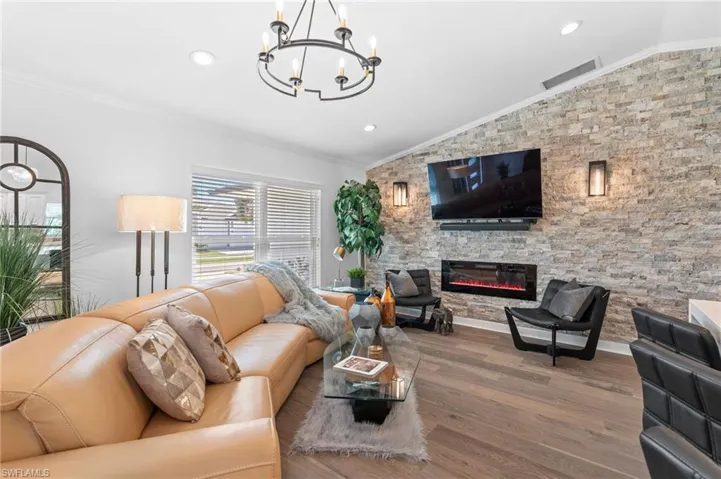 Living room with ornamental molding, wood finished floors, lofted ceiling, a stone fireplace, and recessed lighting