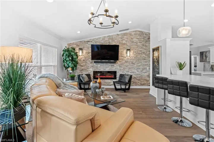 Living room featuring wood finished floors, lofted ceiling, a fireplace, crown molding, and a chandelier
