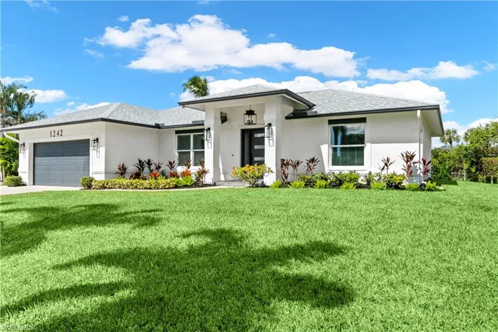 Prairie-style home with an attached garage, stucco siding, a front lawn, and a shingled roof