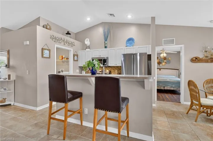 Kitchen with tile patterned floors, decorative backsplash, lofted ceiling, light countertops, and white cabinets
