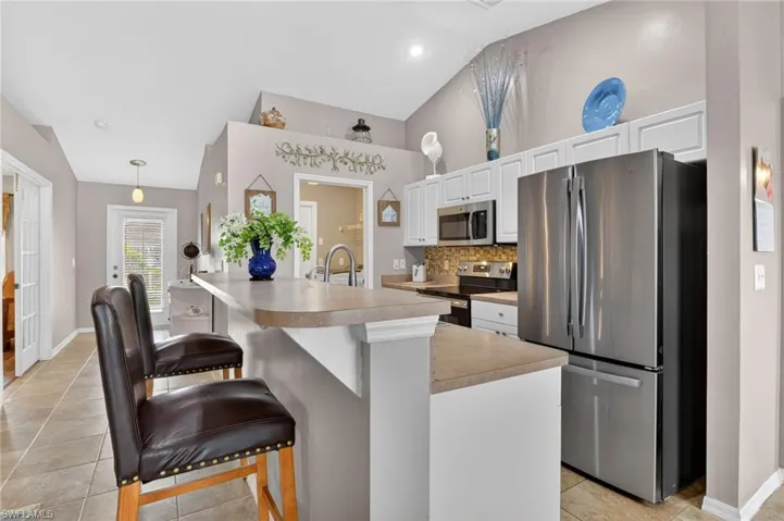 Kitchen featuring stainless steel appliances, white cabinets, a breakfast bar area, pantry, inside laundry access