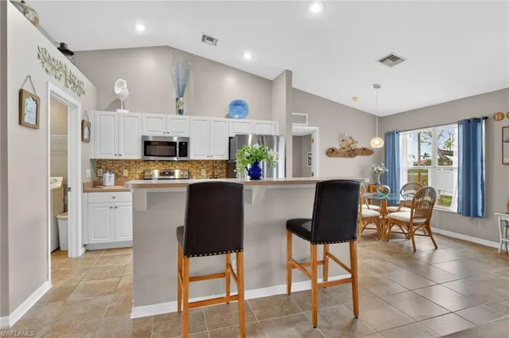 Kitchen with a breakfast bar, light countertops, stainless steel appliances, vaulted ceiling, and white cabinetry