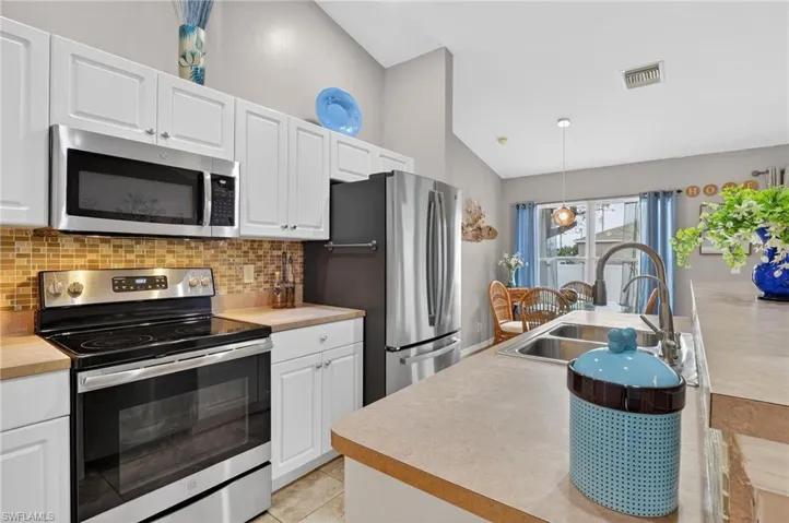 Kitchen featuring stainless steel appliances, white cabinetry, light countertops, vaulted ceiling, and hanging light fixtures