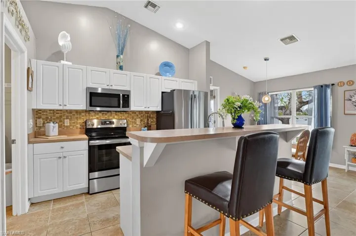 Kitchen with vaulted ceiling, island, stainless steel appliances, white cabinetry, light countertops, and decorative backsplash