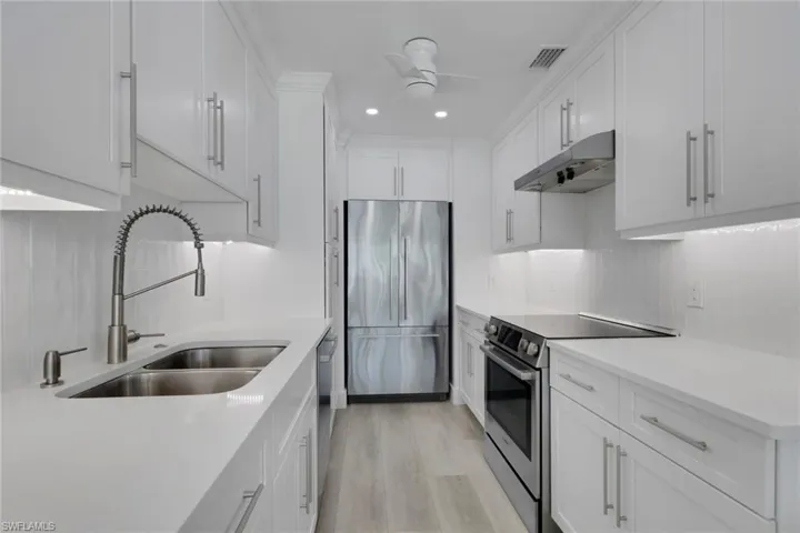 Kitchen with stainless steel appliances, under cabinet range hood, white cabinetry, backsplash, and recessed lighting
