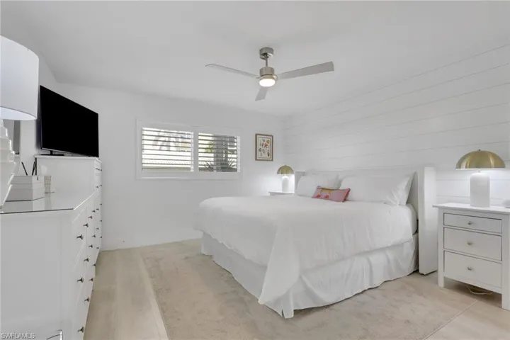 Bedroom with a ceiling fan, wood walls, and light wood-style flooring
