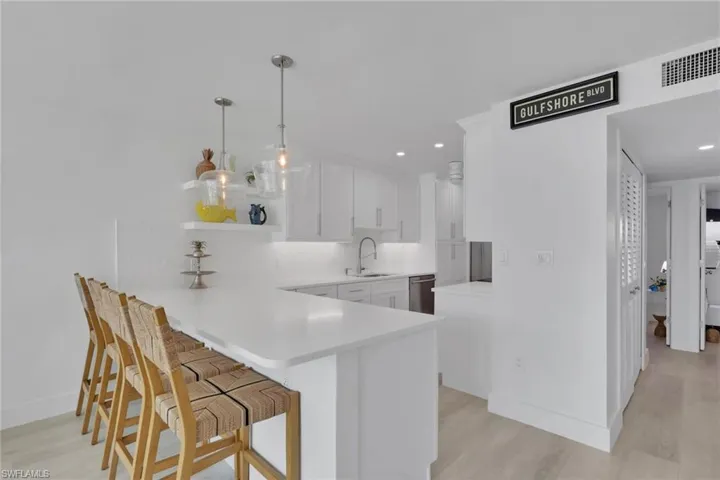 Kitchen featuring a breakfast bar area, a peninsula, white cabinets, open shelves, and hanging light fixtures