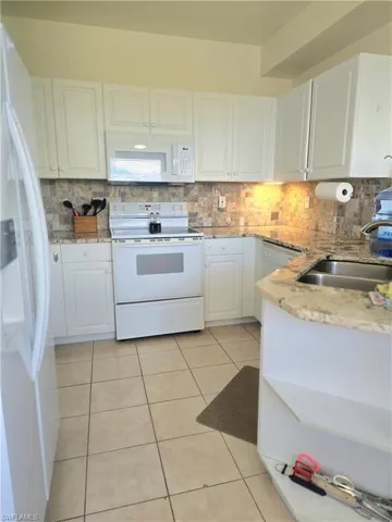 Kitchen with white appliances, light stone countertops, white cabinetry, decorative backsplash, and light tile flooring